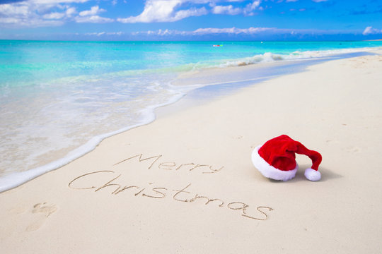 Merry Christmas written on beach white sand with red Santa hat