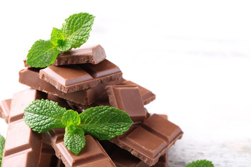 Black chocolate pieces and mint leaves on color wooden background