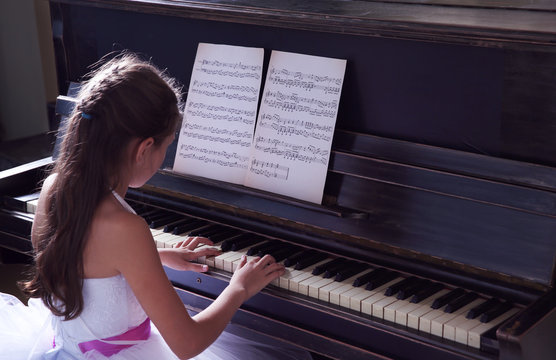 Cute little princess girl plays piano in the studio