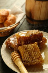 Honeycombs on plate, hot buns in basket on wooden background