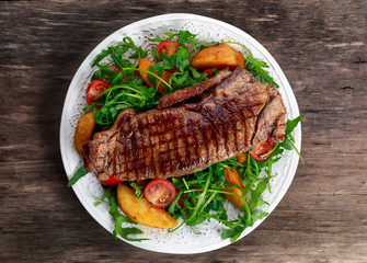 rare beef steak with roasted potatoes, tomatoes and wild rocket leaves. on old wooden table