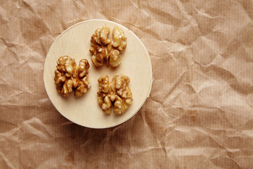 Fototapeta na wymiar Cleaned walnuts on wooden circle on brown craft paper