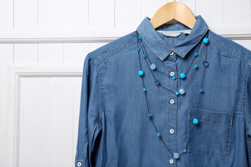 Denim shirt and necklace on hanger on wall background