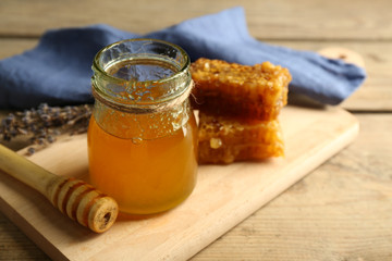 Glass jar with honey, honeycombs and nuts on wooden background
