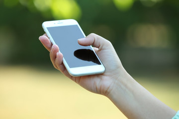 A female hand holding a mobile phone outdoors, on blurred background