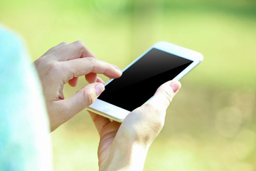 Female hands holding a mobile phone outdoors, on blurred background