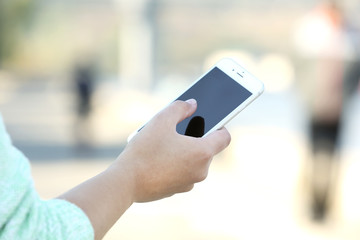 A female hand holding a mobile phone outdoors, on blurred background