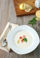 Delicious cream soup with fish and sliced lemon on white table in the restaurant