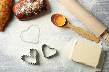 Heart of flour, croissant and  wooden kitchen utensils on gray background