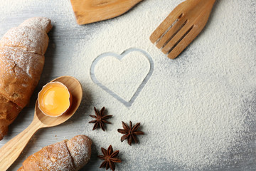 Fototapeta na wymiar Heart of flour, croissant and wooden kitchen utensils on gray background