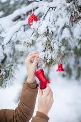 female hands hanging red christmas balls in the winter snowy forest