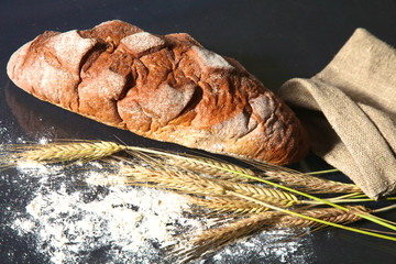 rustic crusty bread and wheat ears on a dark wooden table