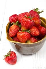 Fresh organic strawberries in bowl on white wooden background