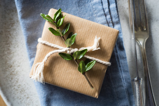 Detail of place setting: simply wrapped present decorated with green branch and twine on the blue napkin