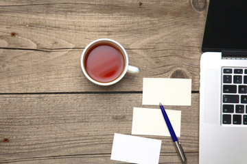 Blank business cards with pen, laptop and tea cup on wooden office table
