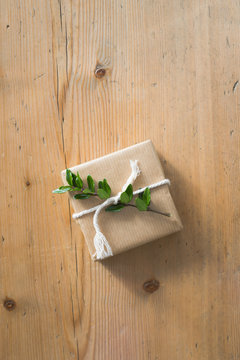 A small present wrapped with kraft paper and decorated with evergreen plant and twine. Wooden backgrounds