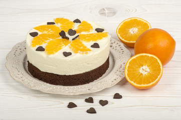  Brownie cake with cream and oranges on the white wooden background.