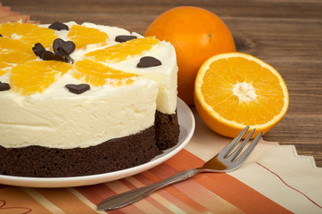 Brownie cake with cream and oranges on the wooden background.