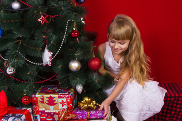 Beautiful baby girl sitting  near the Christmas tree in New Year's Eve smiling and holding a gift