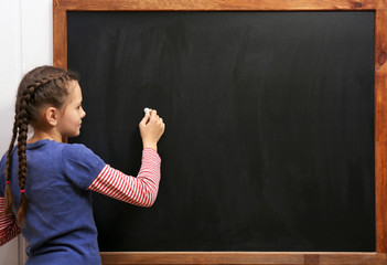 Cute girl posing at the clean blackboard, in the classroom
