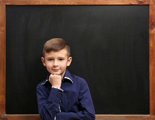 Cute boy posing at the clean blackboard, in the classroom