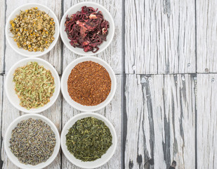 Dried herbal tea leaves, lavender, rooibos, chamomile, linden flower, hibiscus, Japanese green tea in white bowl over wooden background