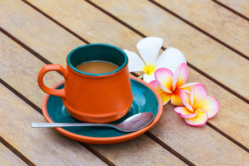 Hot coffee in clay cup and Plumeria flower on the wooden table.