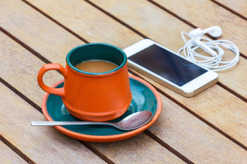 Hot coffee and smart phone and headphone on the wooden table. Focus on a cup.