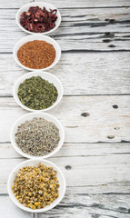 Dried herbal tea leaves, lavender, rooibos, chamomile, linden flower, hibiscus, Japanese green tea in white bowl over wooden background
