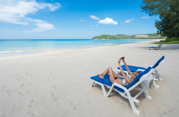 Tropical vacation. Young beautiful woman relaxing alone on the beach and make selfie with smartphone. 