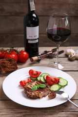 Roasted beef fillet and fresh vegetables on plate, on wooden background