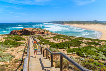 Young woman tourist on walkway to Praia do Bordeira beach and beautiful blue sea view, Algarve region, Portugal