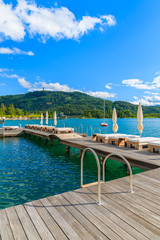 Sunchairs on wooden pier and view of beautiful alpine lake Worthersee in summer, Austria