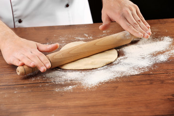 Hands rolling dough basis for pizza on the wooden table, close-up