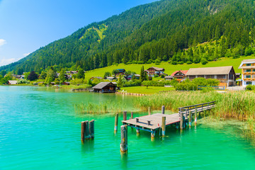 Wooden pier and houses on shore of beautiful Weissensee alpine lake in summer landscape of Alps Mountains, Austria