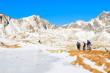 Group of tourists walking along frozen lake in Hincova valley in winter landscape of Tatra Mountains, Slovakia