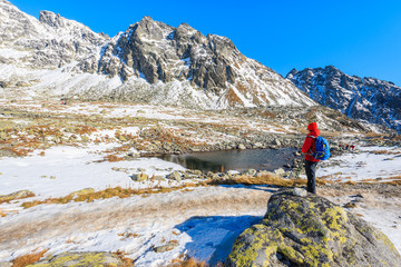 Fototapeta premium Young woman backpacker tourist standing in Hincova valley and looking at mountains covered with snow, Tatra Mountains, Slovakia