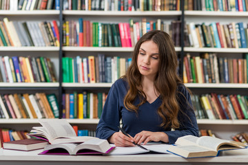 A young brunette girl who is sitting at a desk in the library wi