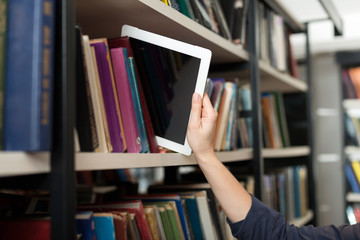 a tablet put with a hand on a book shelf in the library, a conce