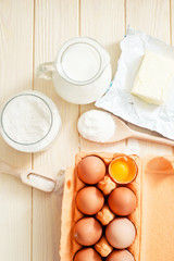 
the ingredients for the dough , eggs , milk, butter , salt and flour on a wooden background
