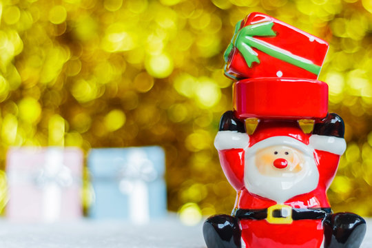 Santa Claus carrying a red gift box and blurred golden sparking bokeh background