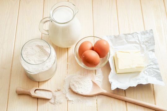 
the ingredients for the dough , eggs , milk, butter , salt and flour on a wooden background