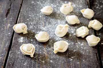 Raw pelmeni dumplings on a dark wooden table, selective focus