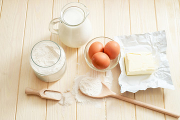 
the ingredients for the dough , eggs , milk, butter , salt and flour on a wooden background