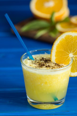 Delicious orange juice in glass and orange next to it on  blue  wooden background