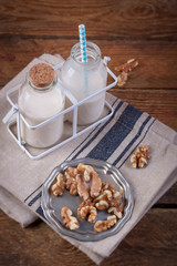 Homemade walnut nut milk in glass bottles with blue straw on a wooden background..