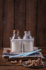 Obraz na płótnie Canvas Homemade walnut nut milk in glass bottles with blue straw on a wooden background.