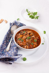 Chicken ragout with pumpkin, mushrooms and oregano stewed in red wine in a white ceramic bowl..