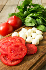 Mozzarella, tomatoes and basil on cutting board
