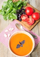 Fresh tomato soup with basil and tomatoes on wooden table